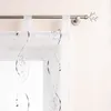 A close-up view of a white sheer curtain with embroidered grey swirls and beads, hanging from a metal curtain rod with a decorative branch-like finial. Produktbild-Vorschau