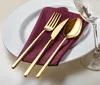 A place setting with gold cutlery on a burgundy napkin on a white plate. Náhľad obrázku produktu