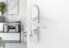 A close-up of a silver door handle with keys inserted into the lock, mounted on a white door. The background shows a blurred interior of a room with furniture. Produktbild-Vorschau