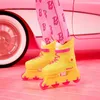 A close-up shot of yellow roller skates with pink accents, worn by a doll, with a pink car and pink floor in the background. Produktbild-Vorschau