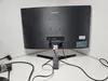 The back of a Samsung monitor is shown on a white desk against a textured white wall. Produktbild-Vorschau