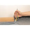 A hand is using a utility knife to cut carpet next to a wooden baseboard. Produktbild-Vorschau