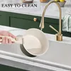 A person is washing a pot in a sink under a golden faucet. Produktbild-Vorschau
