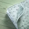 A close-up view of a folded white electric blanket with a gray circular pattern, resting on a light green wooden surface. Náhľad obrázku produktu