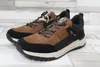 A pair of brown and black sneakers on a light-colored wooden floor. Voir les images du produit