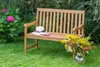 A wooden garden bench in a garden setting with flowers and a hat on it. Produktbild-Vorschau