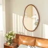 A bedroom scene with a mirror above a headboard, featuring a vase of flowers on a nightstand. Produktbild-Vorschau