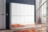 A modern white wardrobe with mirrored doors is shown in a room with a spiral staircase and a colorful rug. Produktbild-Vorschau