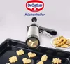 A cookie press with freshly baked cookies on a baking tray and a plate. Anteprima dell’immagine prodotto