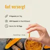 A hand holding a turmeric capsule, with turmeric roots and powder in the background, and text describing product details. Produktbild-Vorschau