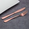 A copper-colored knife and fork are placed on a gray surface next to a white plate. Voir les images du produit