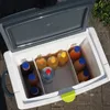 An open cooler box filled with various bottles of drinks, placed outdoors on a paved surface. Produktbild-Vorschau