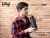 A young person holding a black water bottle in front of a brick wall. Produktbild-Vorschau