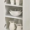 Interior view of a white cabinet with shelves holding various kitchenware. Produktbild-Vorschau