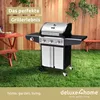 A gas grill is set up on a grassy lawn in front of a wooden fence. Produktbild-Vorschau
