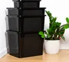 A stack of four black storage boxes with textured panels, placed in a corner next to a potted plant. Podgląd zdjęcia produktu