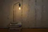 A desk lamp with a filament bulb sits on a stack of books next to a textured wall. Produktbild-Vorschau