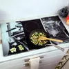 A kitchen counter with a glass stovetop cover featuring a black and white image of a coffee machine. A frying pan with vegetables is on the stovetop. Podgląd zdjęcia produktu