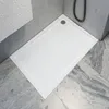 A white shower tray is shown in a bathroom setting with gray tiled walls and floor. Produktbild-Vorschau