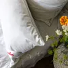 Two pillows on a bed with a small vase of flowers on a side table. Produktbild-Vorschau