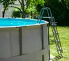 An above-ground swimming pool with a ladder, set up in a grassy backyard on a sunny day. Produktbild-Vorschau