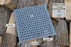 A square metal grate with many holes is placed on a pile of firewood. Dimensions and model information are overlaid on the image. Produktbild-Vorschau