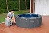 A man is setting up an inflatable hot tub in a backyard patio area. Produktbild-Vorschau