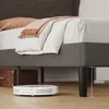 A close-up view of a bed frame with bedding and a robot vacuum cleaner underneath. Náhled obrázku produktu