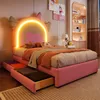 A pink children's bed with a winged headboard and LED lighting, set in a bedroom with a bookshelf and artwork. Produktbild-Vorschau