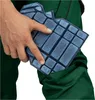 A hand is holding a blue knee pad over a green work pant pocket. Produktbild-Vorschau