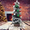 A small, decorated Christmas tree sits on a wooden table in front of a fireplace. Produktbild-Vorschau