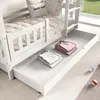 A white wooden bunk bed with a pull-out drawer containing folded clothes. The bed has a quilted mattress and decorative pillows. Produktbild-Vorschau