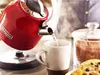 A red electric kettle pouring hot water into a mug, next to a jar of cocoa and a cookie. Produktbild-Vorschau