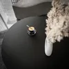 A close-up overhead view of a round black coffee table with a cup of coffee and a vase of dried flowers. Produktbild-Vorschau