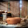 A rustic scene with a terracotta pot, bread, and garlic on a table. Voir les images du produit