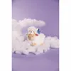 A plush sheep toy sitting on fluffy white material resembling clouds, against a purple background. Anteprima dell’immagine prodotto