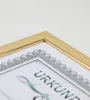 A close-up shot of a gold-colored picture frame holding a certificate or document. Produktbild-Vorschau