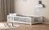 A white wooden children's bed with a guardrail is set up in a nursery or child's bedroom. Decorative clouds and a koala figure are on the wall behind the bed. Toys are scattered on a rug in the foreground. Anteprima dell’immagine prodotto