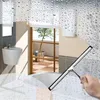 A hand holding a squeegee cleaning a shower wall with water droplets. Podgląd zdjęcia produktu