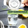 Juice being poured from a stainless steel juicer into a glass of water, with lemons in the background. Produktbild-Vorschau