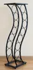 A black metal wine rack with a curved design, standing on a wooden floor against a light-colored wall. Anteprima dell’immagine prodotto