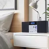 A stereo system is placed on a white nightstand next to a bed, with a lamp and a plant in the background. Produktbild-Vorschau