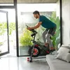 A man is riding an indoor cycling bike in a modern, well-lit room with large windows and plants. Voir les images du produit