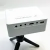 A white mini-projector is mounted on a black tripod, shown from a slightly angled front view against a white background. Produktbild-Vorschau