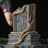 A close-up of a statue base with vines and a carved figure, with a person's leg visible on the left. Anteprima dell’immagine prodotto