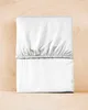 A white fitted sheet is folded and placed on a light brown wooden surface. Anteprima dell’immagine prodotto