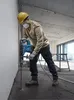 A construction worker is using a rotary hammer drill to drill into a concrete floor. Produktbild-Vorschau