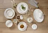A collection of white porcelain dinnerware with gold trim, arranged on a wooden table. Produktbild-Vorschau