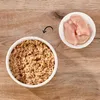 A bowl of shredded food and a bowl of raw chicken pieces are shown on a wooden surface, with an arrow indicating a transition. Produktbild-Vorschau