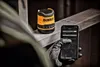 A person wearing gloves is using a smartphone to connect to a DeWalt Bluetooth speaker. Podgląd zdjęcia produktu